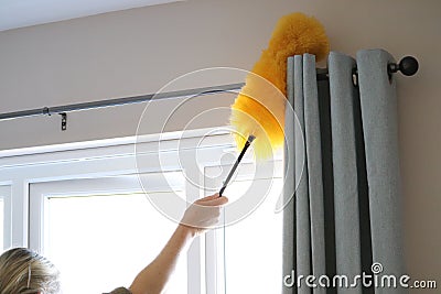 Cleaning the window and curtains area with a fluffy yellow duster Stock Photo