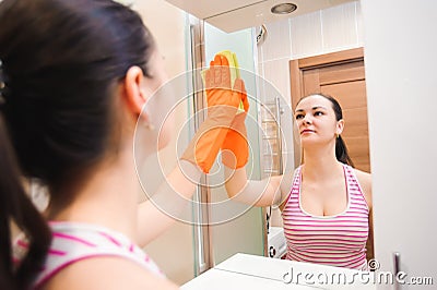 Cleanness in every move. Pretty brunette cleans mirror with help of yellow cloth and special mean of cleaning Stock Photo