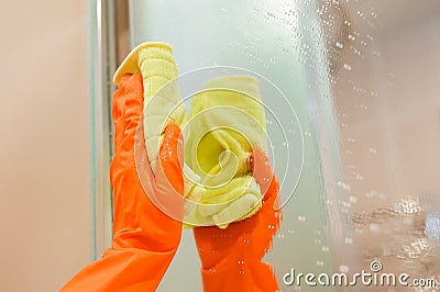 Cleanness in every move. Pretty brunette cleans mirror with help of yellow cloth and special mean of cleaning. Stock Photo