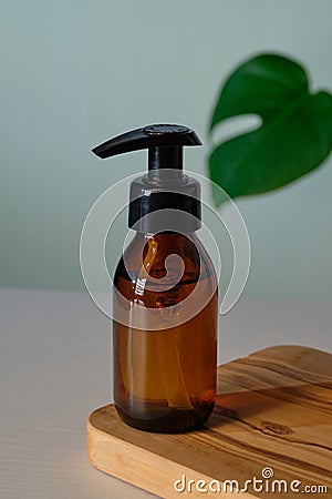 Clear amber glass pump bottle mockup with tropical green leaf. Dispenser packaging design for natural organic cosmetics Stock Photo