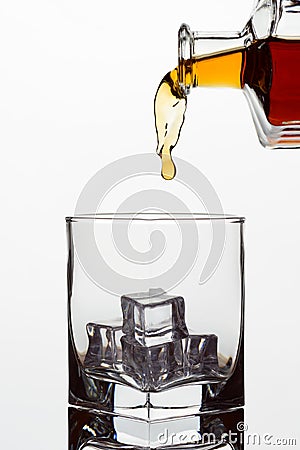 Clear glass glass with ice cubes. Frozen stream from a bottle of whiskey or cognac or brandy on a white isolated background Stock Photo