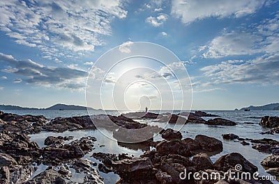 Clear sky white clouds on sunny day and rocks in the foreground, silhouette fishing man on stones seashore under a blue summer sky Stock Photo