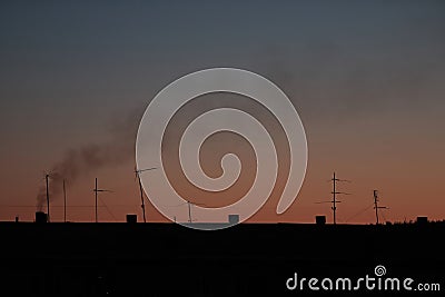 Clear sunrise or sunset sky with a smooth gradient of colors. Dark silhouettes of the roof of the building with antennas and pipes Stock Photo