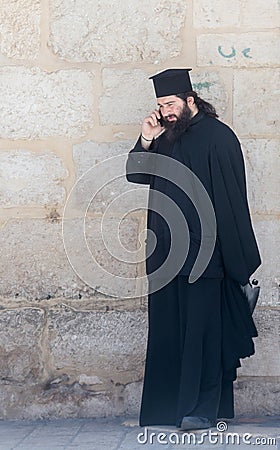 The clergyman stands and talks on his mobile phone in the old city of Jerusalem, Israel. Editorial Stock Photo