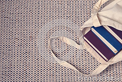 Clever weighty books in textured blue and lilac fabric covers lie in an open linen bag. Stock Photo