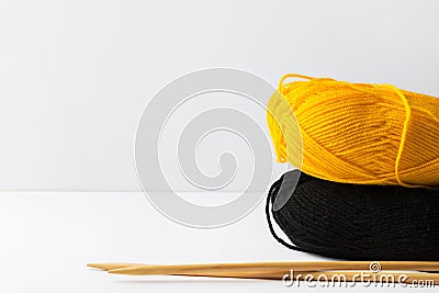 Clews of yellow black fine wool yarn wooden knitting needles on white table on wall background warm autumn color palette. Crafts Stock Photo