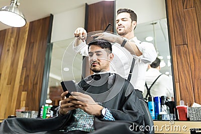 Client Using Smartphone While Hairdresser Giving Him A Haircut Stock Photo