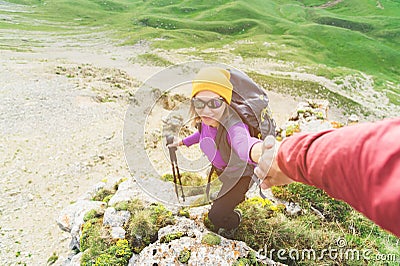 A climber helps a young mountaineer woman reach the top of the mountain. A man gives a helping hand to a woman. View Stock Photo