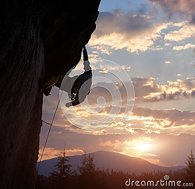 Climber holding with one hand on hanging rock at sunrise in mountains. Extreme rock climbing. Cloudy sky with copy space Stock Photo