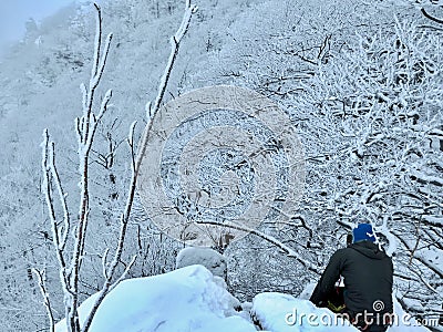 Climber is sitting on the top of the rock covered with snow belaying his friend. Stock Photo