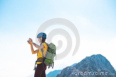 climber on top of the mountain takes a photo. Girl with a backpack and hard hat in the mountains. Woman traveler takes a photo on Stock Photo