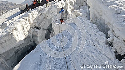 A climber walks along a narrow mountain dangerous snow-covered path past large cracks and cliffs. Trekking from Camp 2 to Camp 1 Editorial Stock Photo