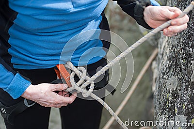 Climber woman in safety harness tying rope in bowline knot Stock Photo