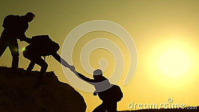 Climbers silhouettes stretch their hands to each other, climbing to the top of the hill. travelers climb one after Stock Photo