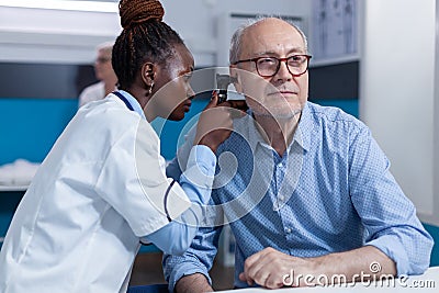 Clinic otology specialist consulting senior patient using otoscope to check ear infection Stock Photo