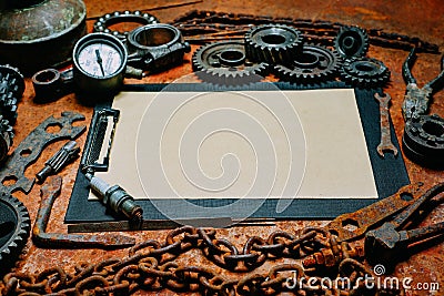 Clipboard with paper in the center of rusty tools, gears on metal background. Motorcycle tools, equipment and repair. Horizontal Stock Photo