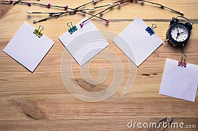 Clips with paper card template, alarm clock, decorative branches on wooden board for text or picture. Paper mockup. Copyspace. Stock Photo