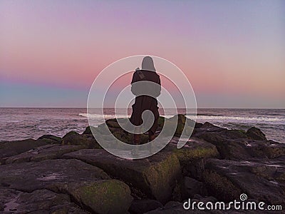 cloaked figure staring out over the ocean from a jetty at sunset Stock Photo