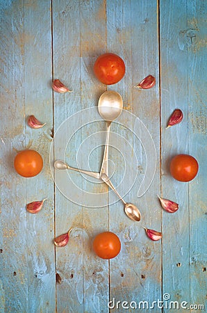 Clock arranged from tomatoes, garlic and spoons. Textured abstract clock face showing 5. Blue background Stock Photo