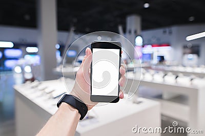 clock hand holds a phone with a white screen against the background of an electronics store Stock Photo