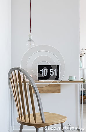 Clock screensaver on a laptop in bright home office interior with wooden chair, simple desk and bare light-bulb. Real photo Stock Photo