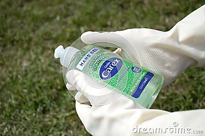 Close angle of a person`s hands wearing beige colored gloves holding the `carex` antibacterial gel. Editorial Stock Photo