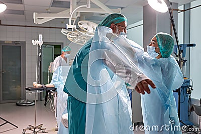 Close doctors team help wearing medical uniform to each other, prepare Stock Photo