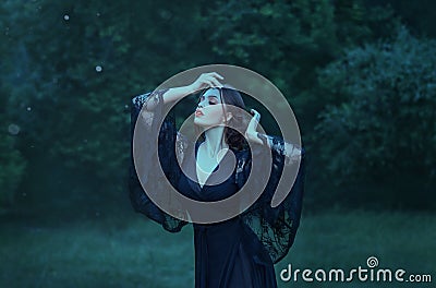 Close eyes, girl dancing in the moon light in the dark emerald forest alone. magic. witch. demon. wearing a black long Stock Photo