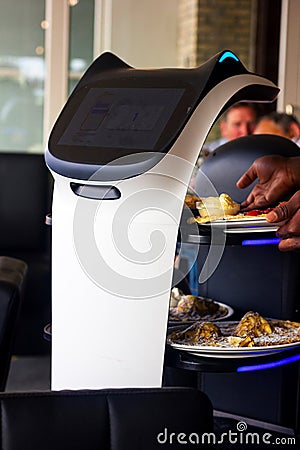 A close portrait of a serving robot on wheels with a screen displaying a cute cat face, riding through a restaurant with plates Editorial Stock Photo