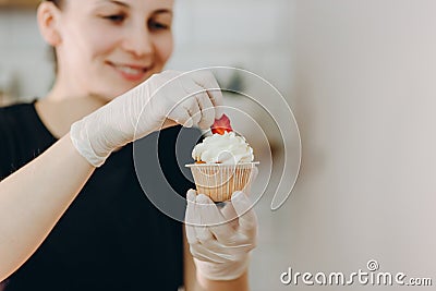 Close shot of many sweet cupcakes on the foreground while a baker decorating the last one. Stock Photo