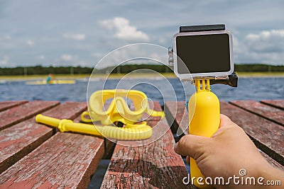 Close-up, action camera mockup with a yellow float in a man`s hand. Against the background of a waterproof mask for snorkeling, Stock Photo