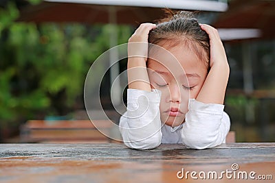 Close-up of adorable little Asian child girl expressed disappointment or displeasure on the wood table Stock Photo