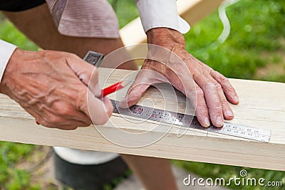 Close-up of adult male hands holding woodworking marking tool - red pencil and metal ruler corner and measures and marks the area Stock Photo