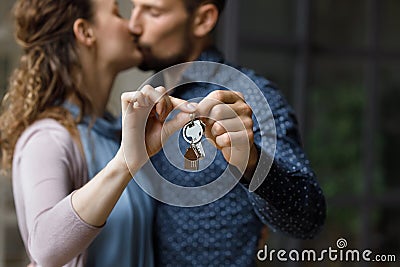 Affectionate kissing millennial couple showing keys to camera Stock Photo