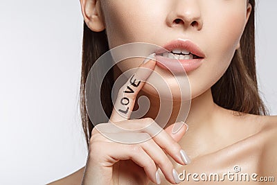 Passionate lady keeping finger with love lettering near mouth Stock Photo