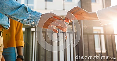 Close up of African American female hand passing key to male outdoors in sunlight. Woman handing keys of new house to Stock Photo