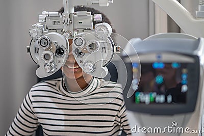 Close-up Of african teen girl Doing Eye Test On Phoropter, African teen girl checking on her eye with optometry machine Stock Photo