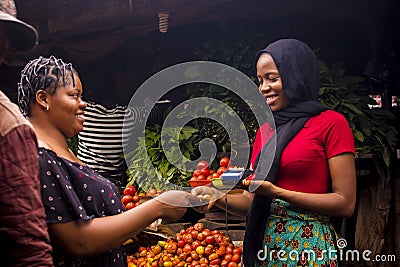 Close up of an african woman selling food stuff in a local african market holding a mobile point of sale device collecting a Stock Photo