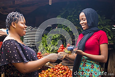 Close up of an african woman selling food stuff in a local african market holding a mobile point of sale device collecting a Stock Photo