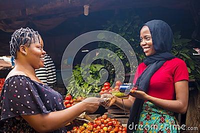 Close up of an african woman selling food stuff in a local african market holding a mobile point of sale device collecting a Stock Photo