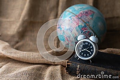 Close up of alarm clock on the old holy bible with blurred world globe on vintage linen sackcloth background Stock Photo