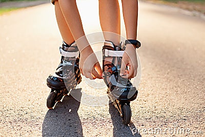 Close-up of an anonymous kid`s hands fixing laces on roller blades before skating, unknown child on road in sunny summer day, Stock Photo