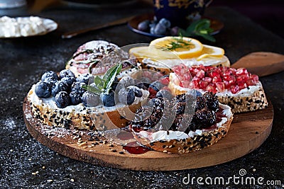 Close-up appetizing bruschetta with cream cheese. Garnished with blueberries, lemon, ripe pomegranate and apple Stock Photo