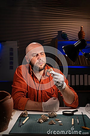 close-up of an archaeologist working at night in the office studying and restoring coins found at the excavations of an Stock Photo