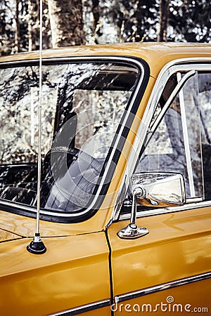 Close up artistic style view of old yellow vintage car front window wheel and antenna outdoors in summer. Stock Photo