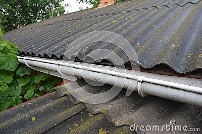 A close-up of an asbestos roof with a plastic roof gutter. An old corrugated asbestos roof Stock Photo