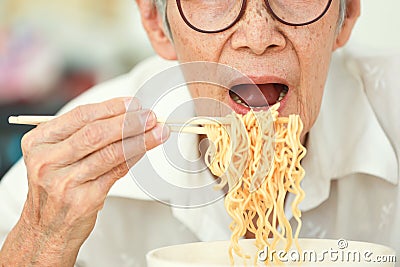 Close up,Asian senior woman opening her mouth to eat instant noodles,junk food,old elderly eating instant noodles,dangers of high Stock Photo