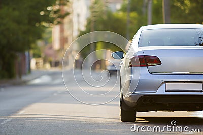 Close-up back view of new shiny expensive silver car moving along city street on blurred trees, cars and buildings background on Stock Photo