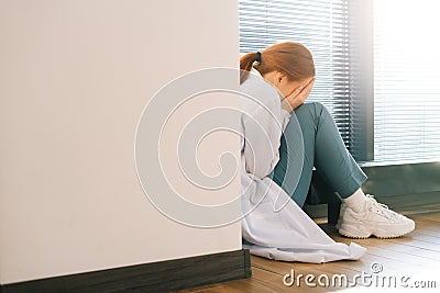 Close-up back view of sad depressed female doctor crying sitting near window holding head and arms on knee. Stock Photo