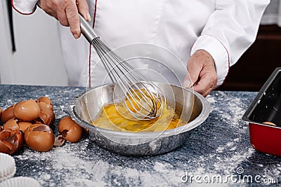 Close-up of a baker mixing eggs with a hand blender in a steel bowl Stock Photo